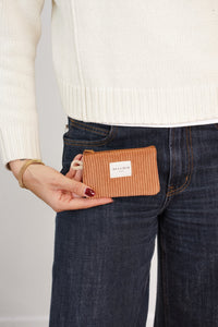 Model holding DE LA MUR terracotta corduroy coin purse at hip, lifestyle shot