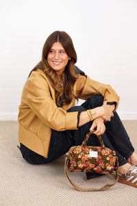 DE LA MUR Floral Jacquard Small Handbag in brown and red held by a seated model
