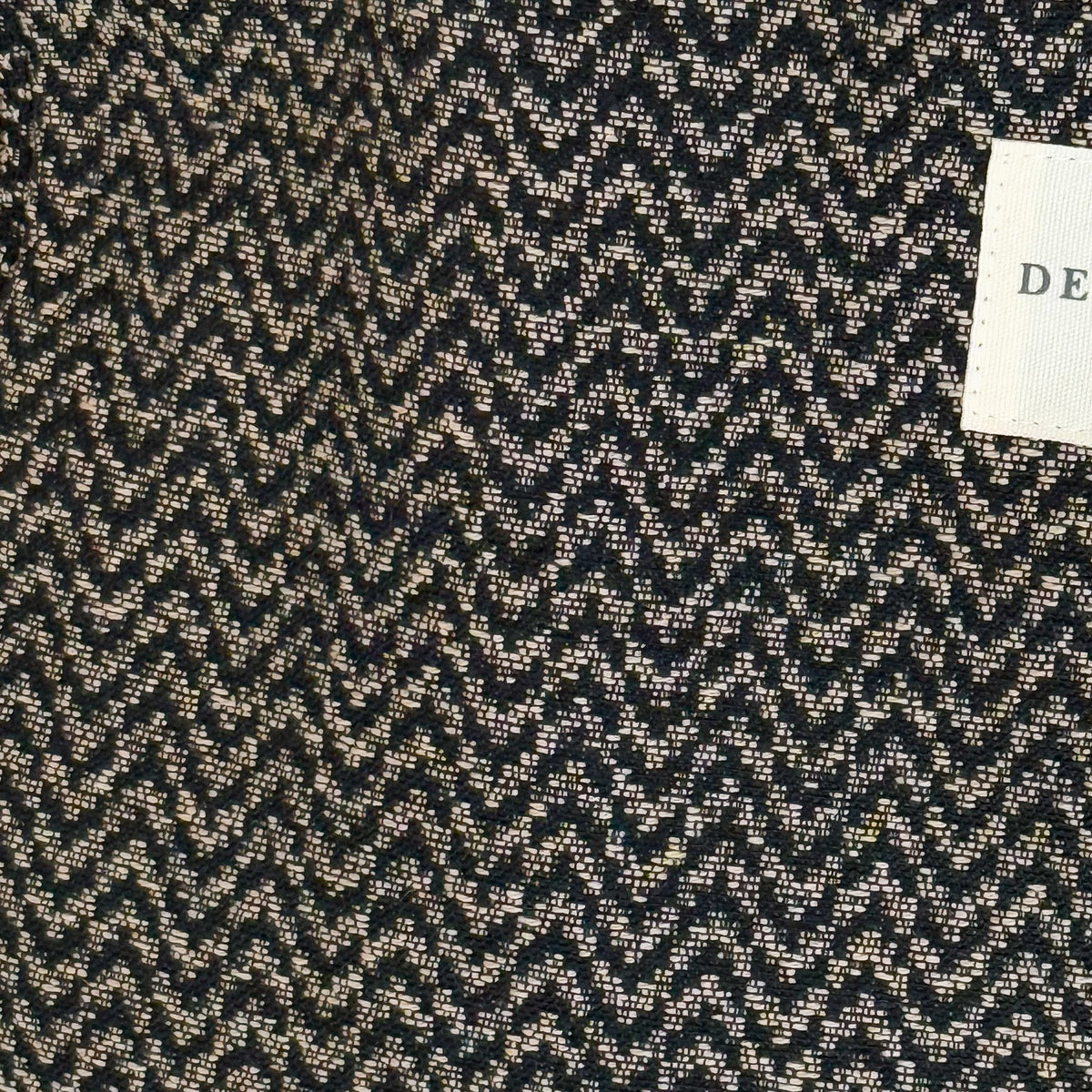 Close-up of the black and beige zigzag jacquard fabric and DE LA MUR Line label