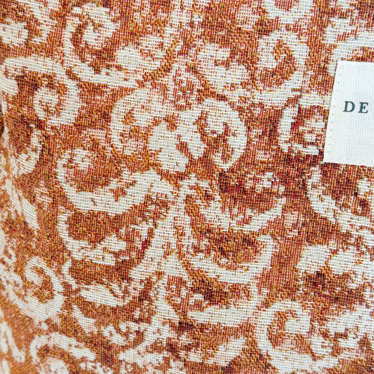 Close-up of the rust geometric jacquard fabric and DE LA MUR label