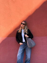 Model carrying the DE LA MUR gray corduroy tote bag against a colorful wall