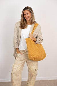 Model carrying DE LA MUR mustard corduroy large zippered bag on the shoulder, lifestyle shot