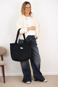 Model carrying the DE LA MUR black corduroy large zippered bag on her arm, lifestyle shot