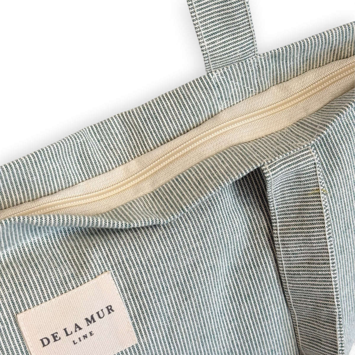 Close-up of the ivory top zip and DE LA MUR Line label on the Teo striped tote