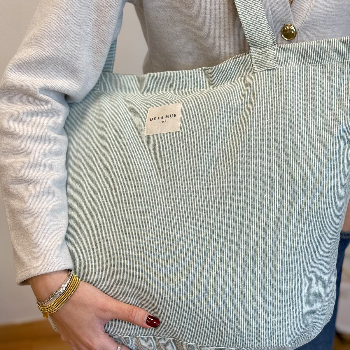 Model carrying the DE LA MUR Teo light green striped tote on the shoulder