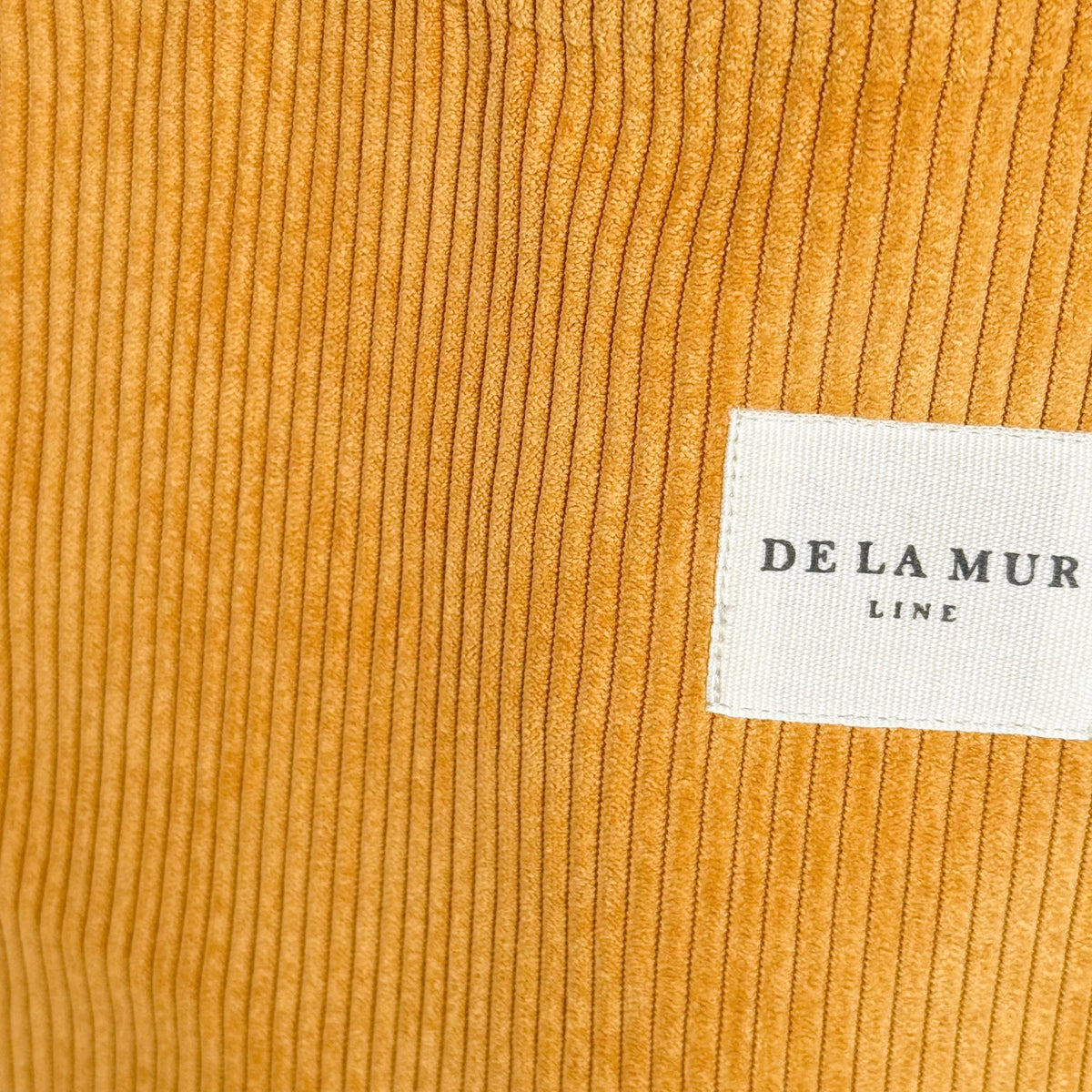 Close-up of mustard corduroy fabric and DE LA MUR Line label