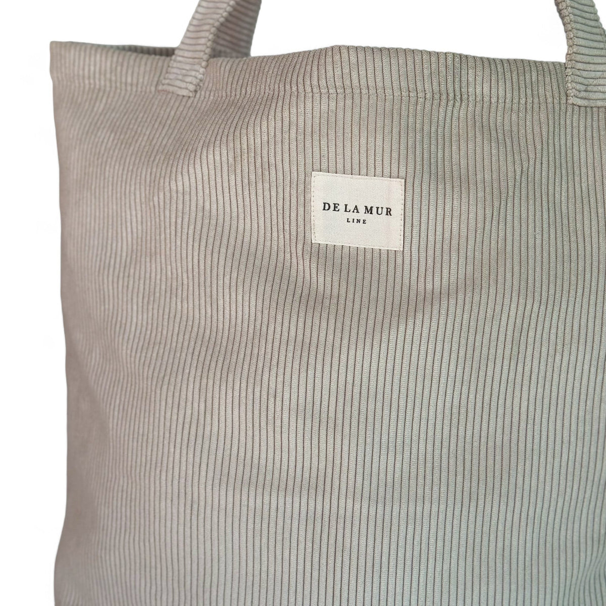 Close-up of beige corduroy texture and DE LA MUR Line label on large tote