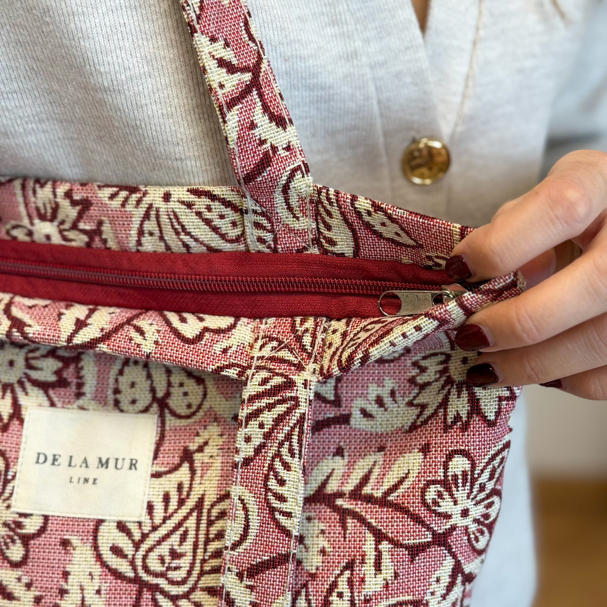 Close-up of the DE LA MUR pink floral bag zip opening, held by a model