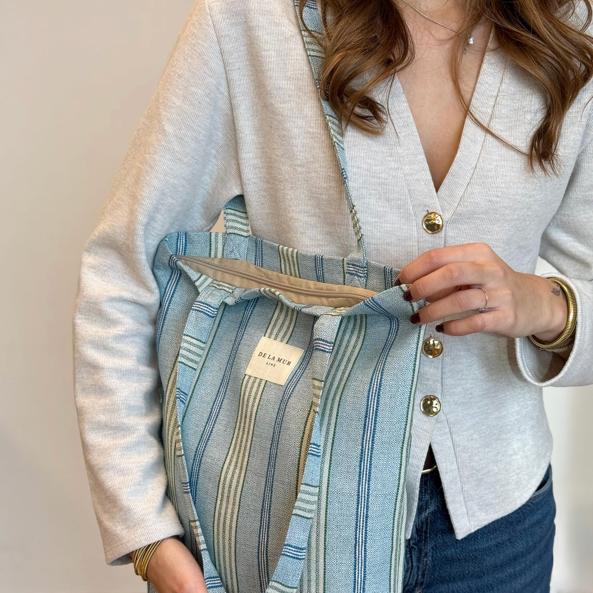 Model opening the DE LA MUR striped bag, showing the lined interior