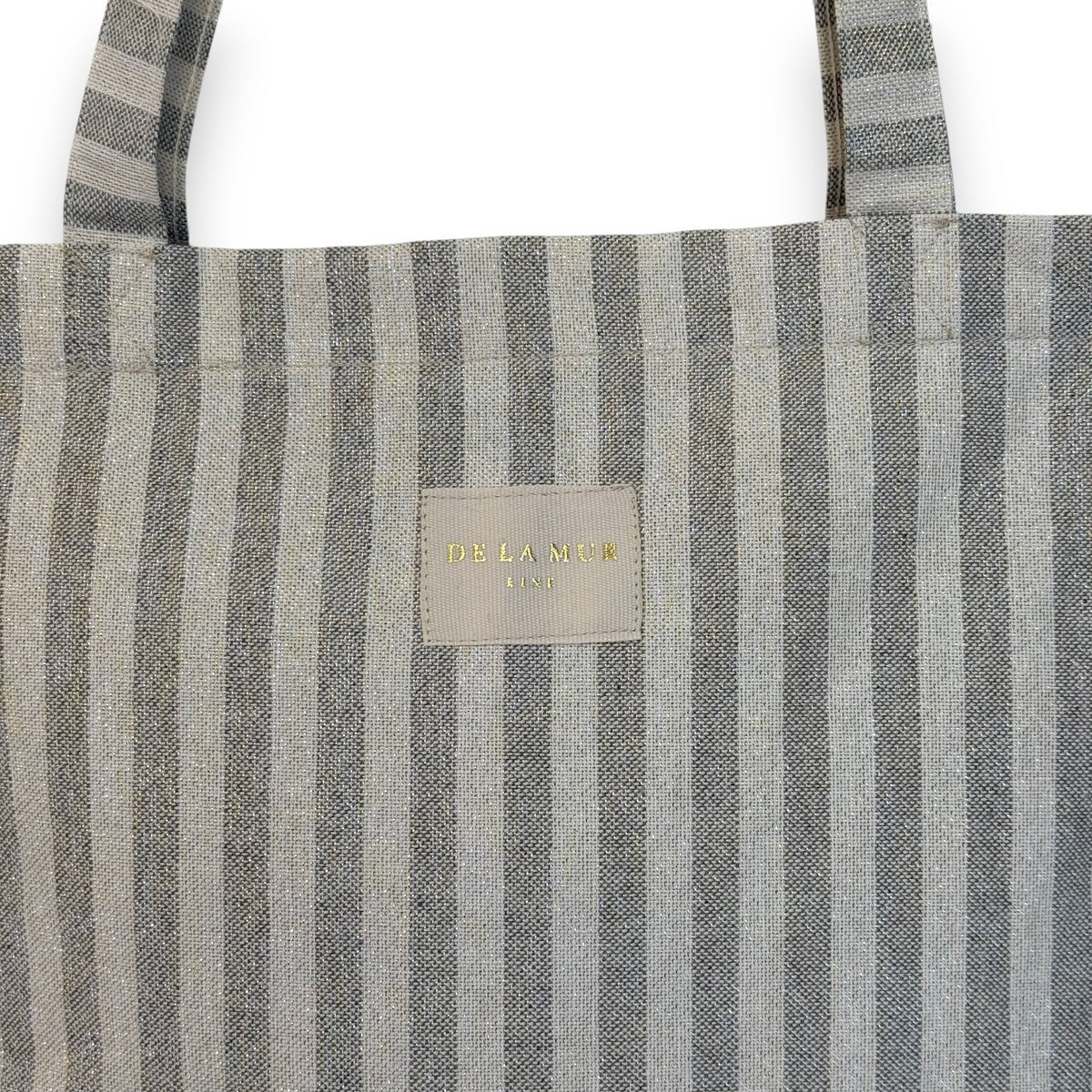 Close-up of the DE LA MUR Lugris gray striped fabric and gold Line label