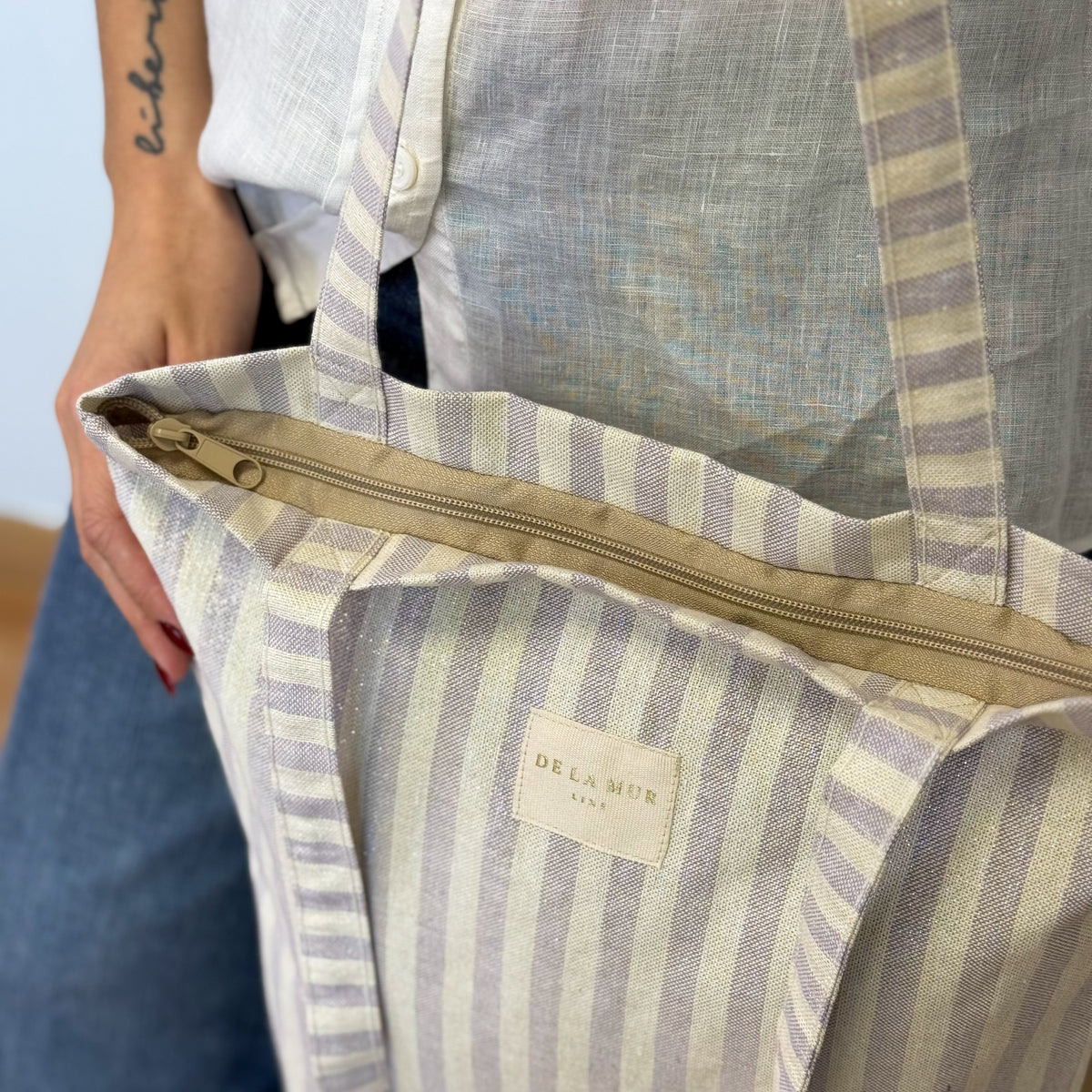 Hands opening the zip of the DE LA MUR Lulil striped bag on the shoulder
