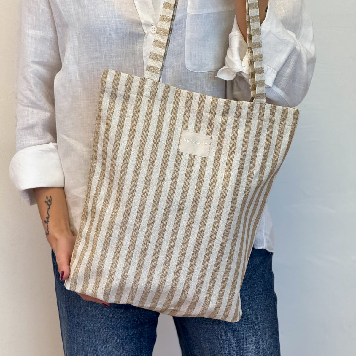 Model carrying the DE LA MUR Lumos mustard and gold striped shoulder bag