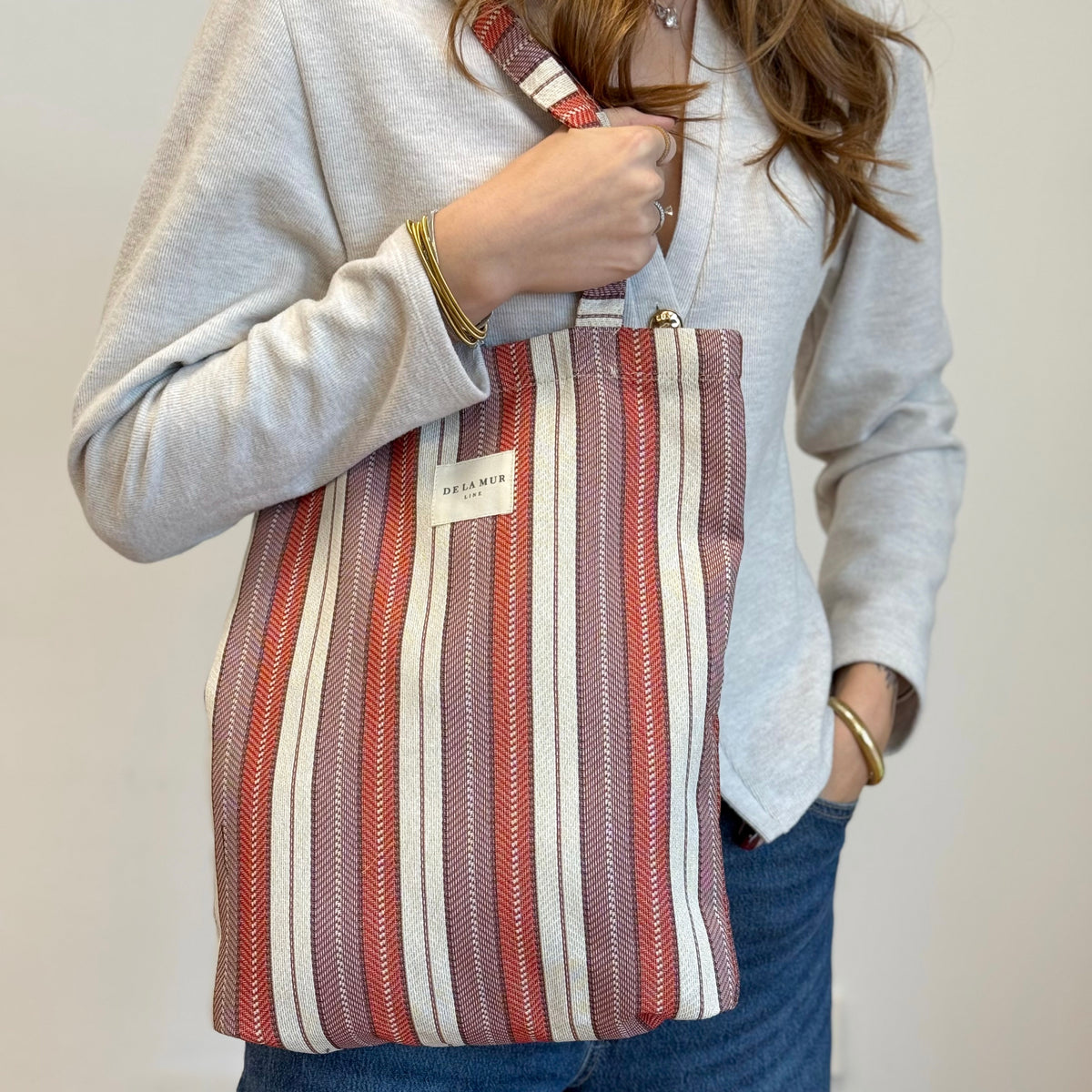 Model carrying the DE LA MUR Make lilac and burgundy striped shoulder bag