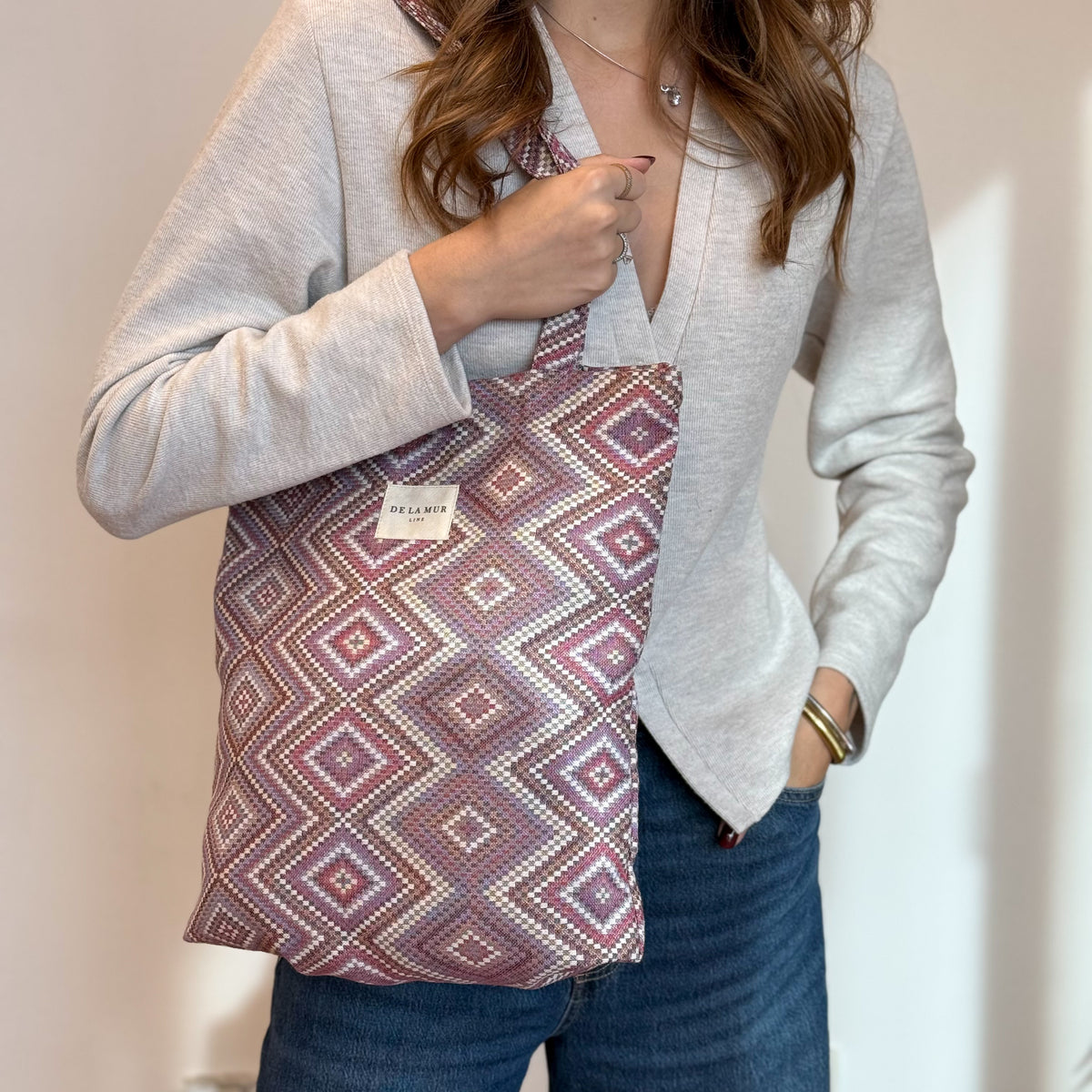 Features infographic of the DE LA MUR Nana geometric jacquard bag with model