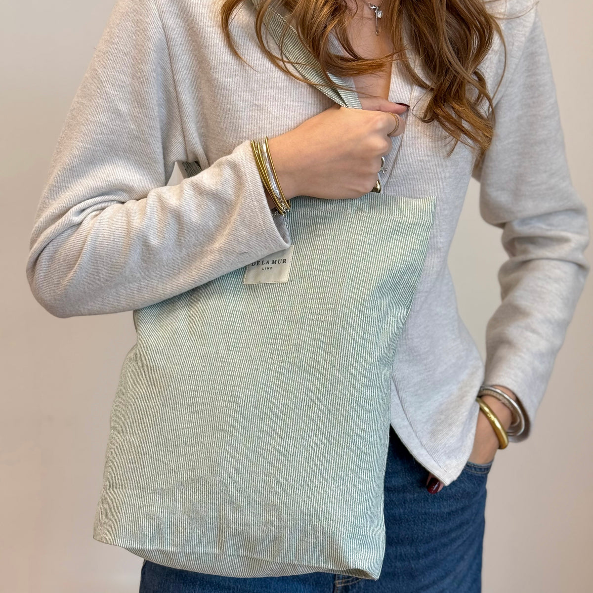 Model holding the DE LA MUR Teo striped tote bag over the shoulder