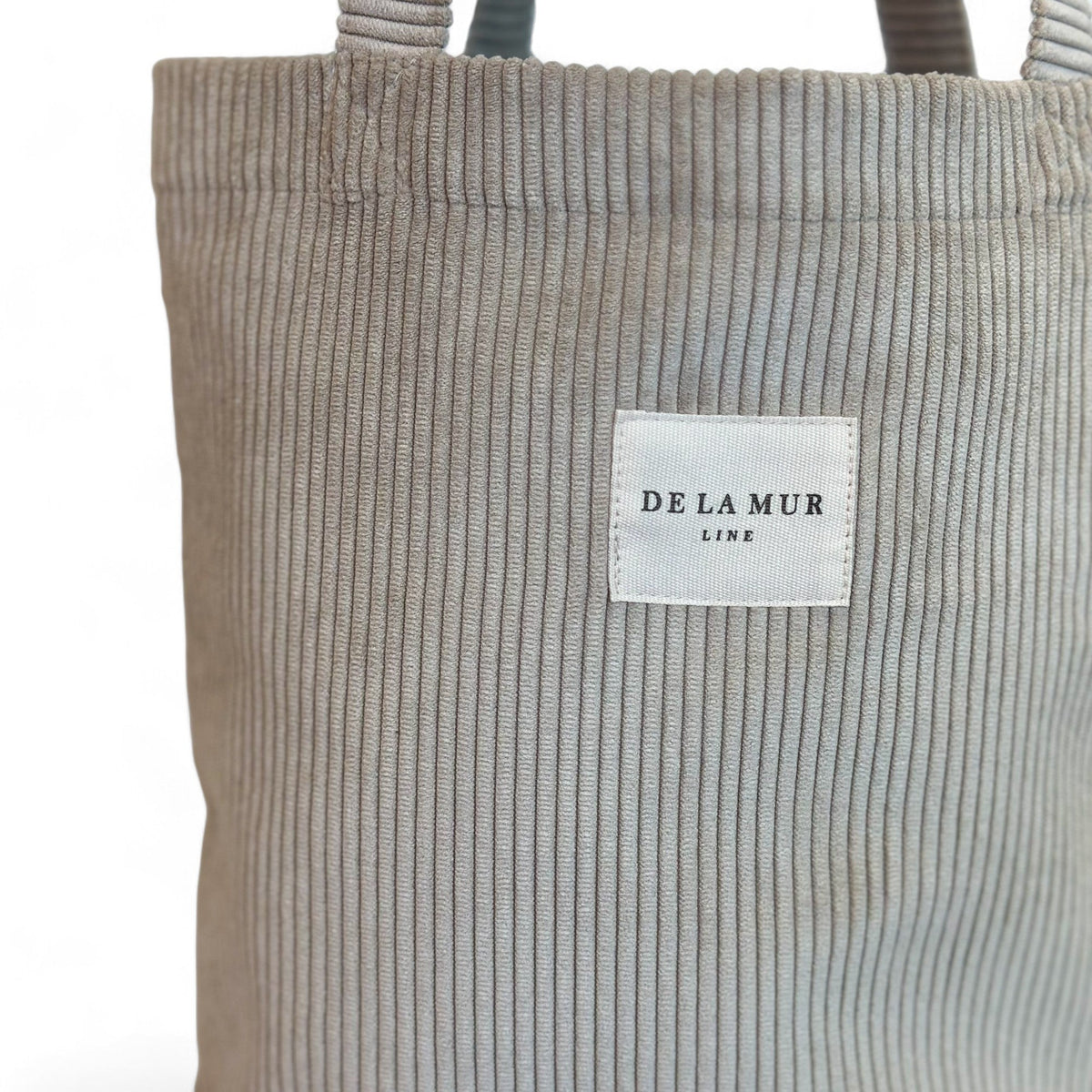 Close-up of beige corduroy fabric and DE LA MUR Line woven label on tote bag