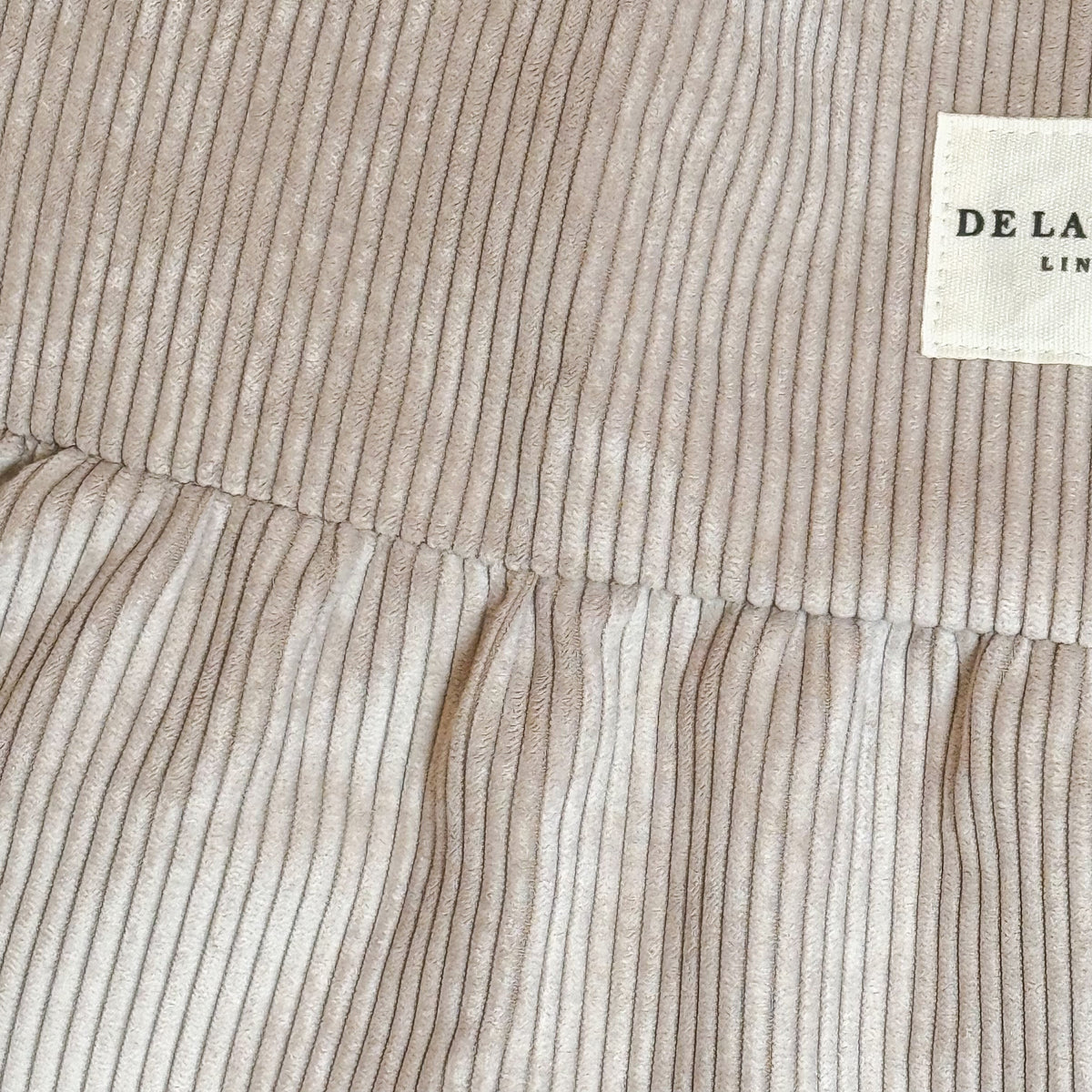 Close-up of the ribbed corduroy fabric and DE LA MUR Line label on the beige tote