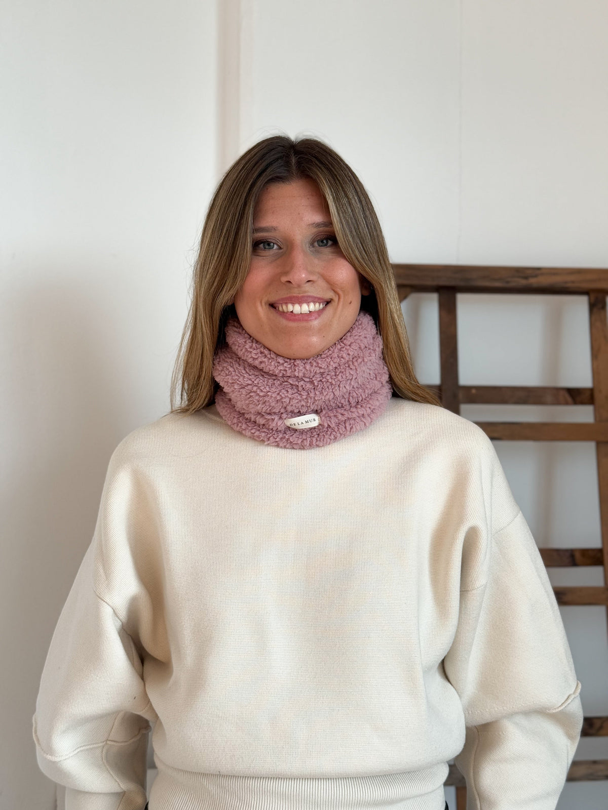 Model wearing the pink DE LA MUR Kalt sherpa neck warmer with cream sweater