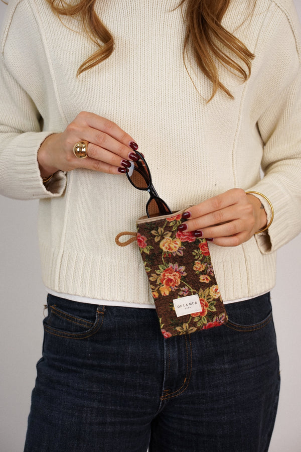 Model tucking glasses into DE LA MUR brown floral jacquard glasses case