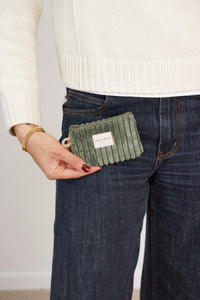 Model holding the DE LA MUR Musgo olive green corduroy coin purse by a jeans pocket