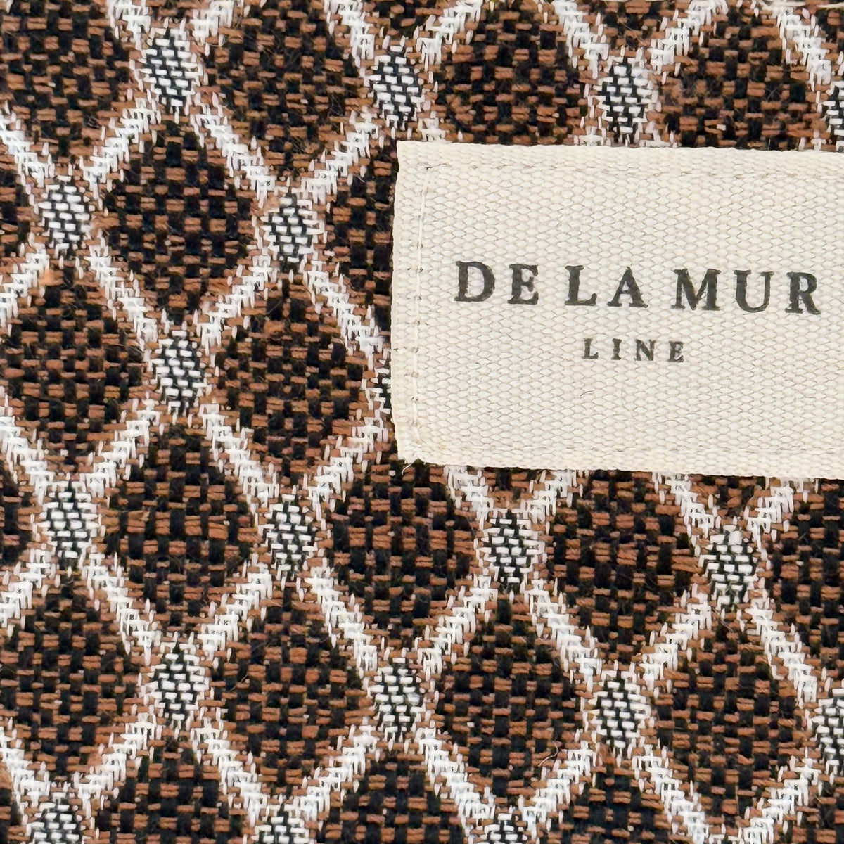 Close-up of the beige and brown lattice jacquard fabric and DE LA MUR Line label