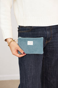 Model holding DE LA MUR teal corduroy makeup bag by the hip, lifestyle shot