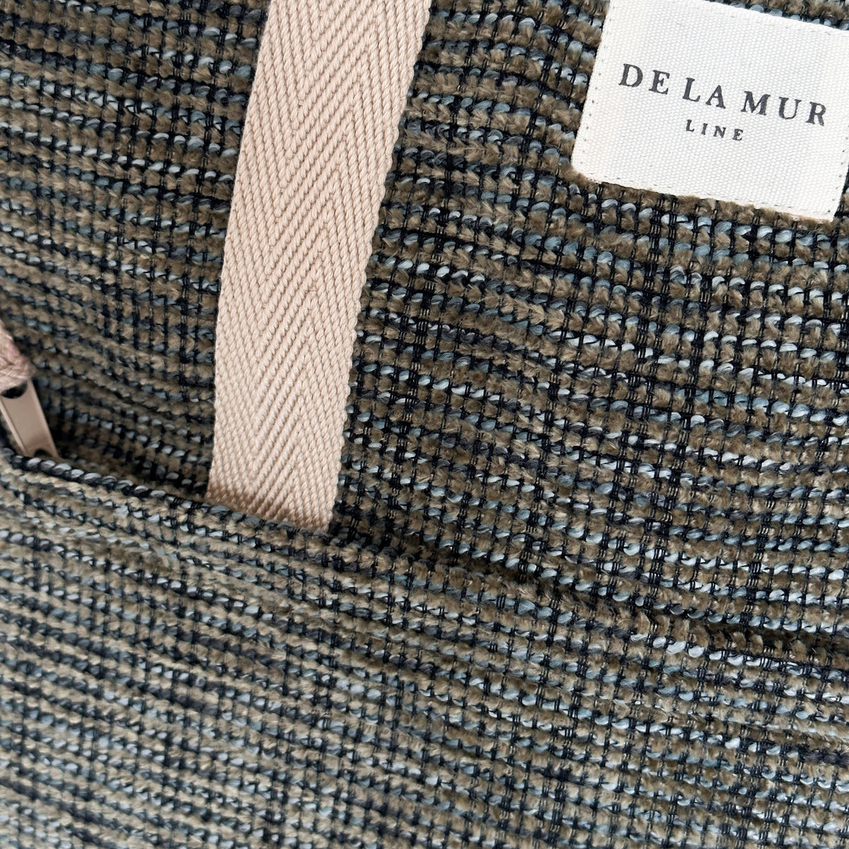Close-up of the khaki green woven fabric and DE LA MUR Line label on the backpack