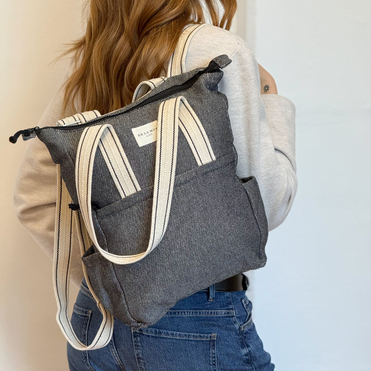 Model wearing the DE LA MUR Sinay herringbone bag as a backpack, back view