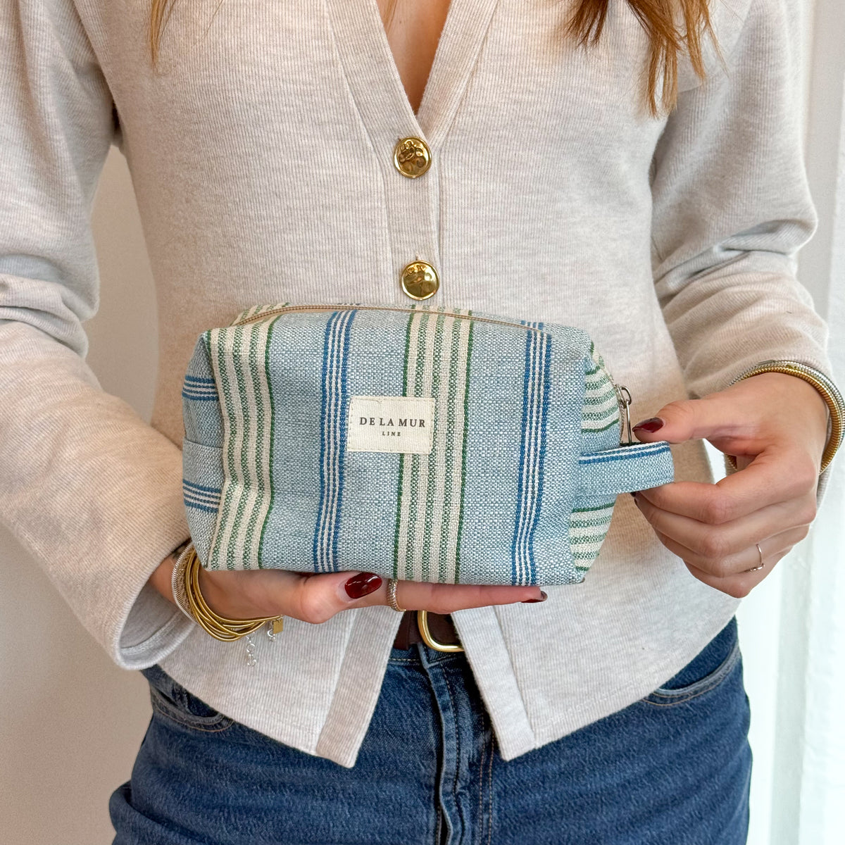 Model holding the blue and green striped DE LA MUR squared makeup bag