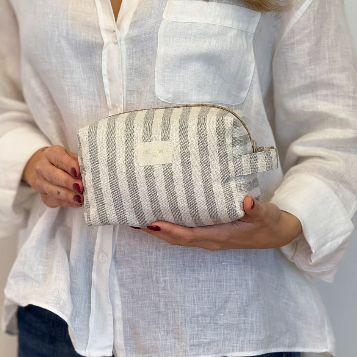 Model holding the DE LA MUR Lugris ecru and gray striped makeup bag