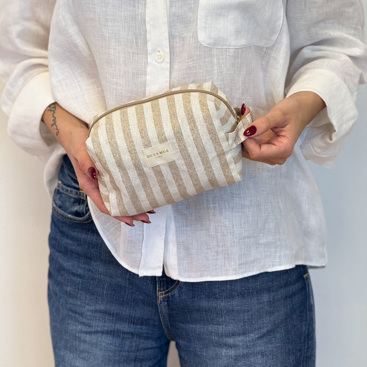 Model holding the DE LA MUR Lumos ecru and mustard striped makeup bag