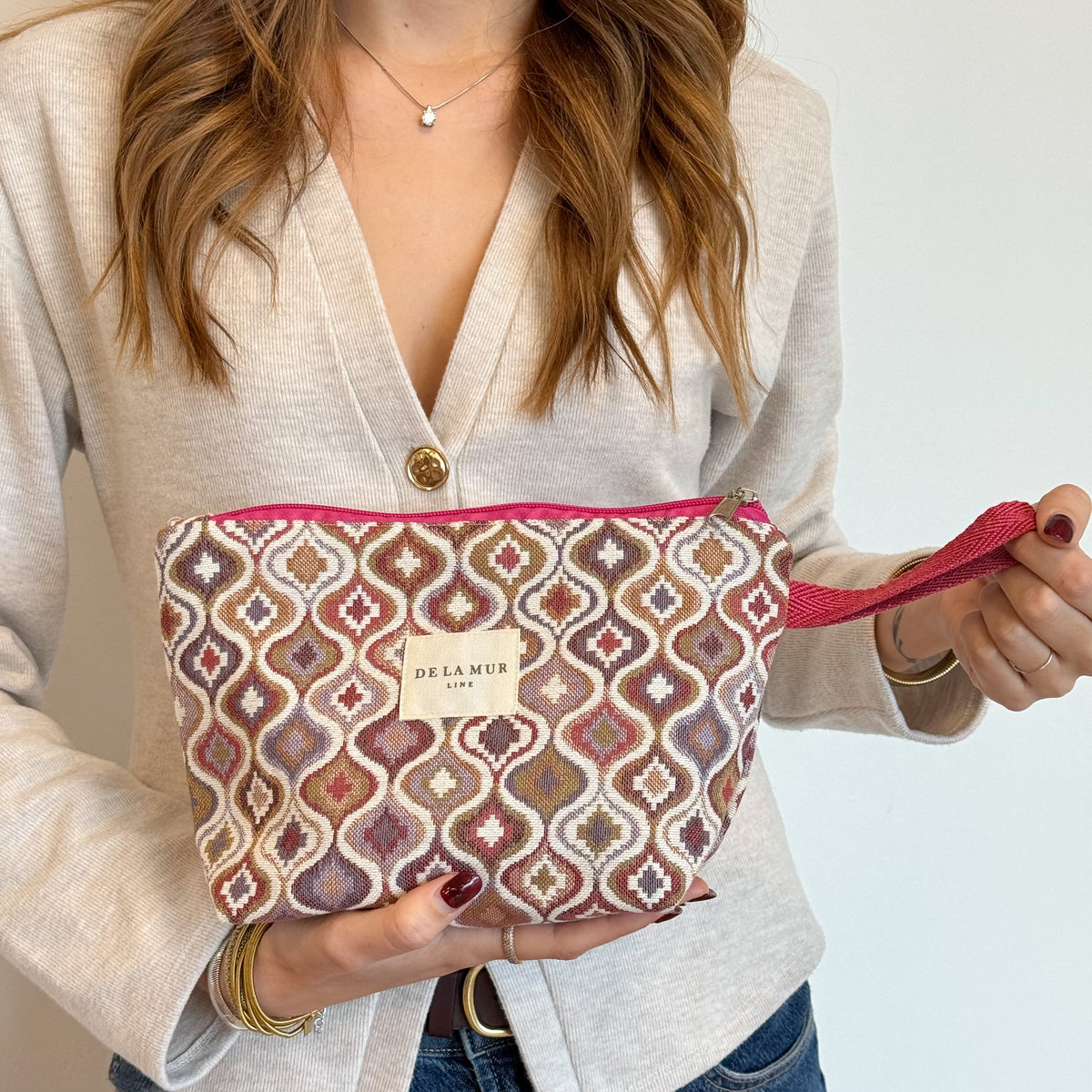 Model holding the ogee-pattern DE LA MUR Onda makeup bag by its pink strap