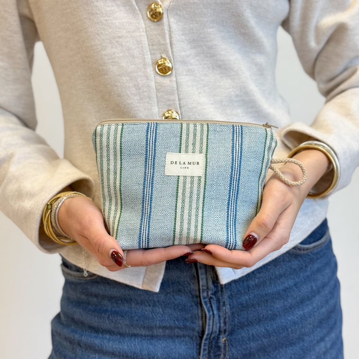 Model holding the DE LA MUR beige and blue striped makeup bag in both hands