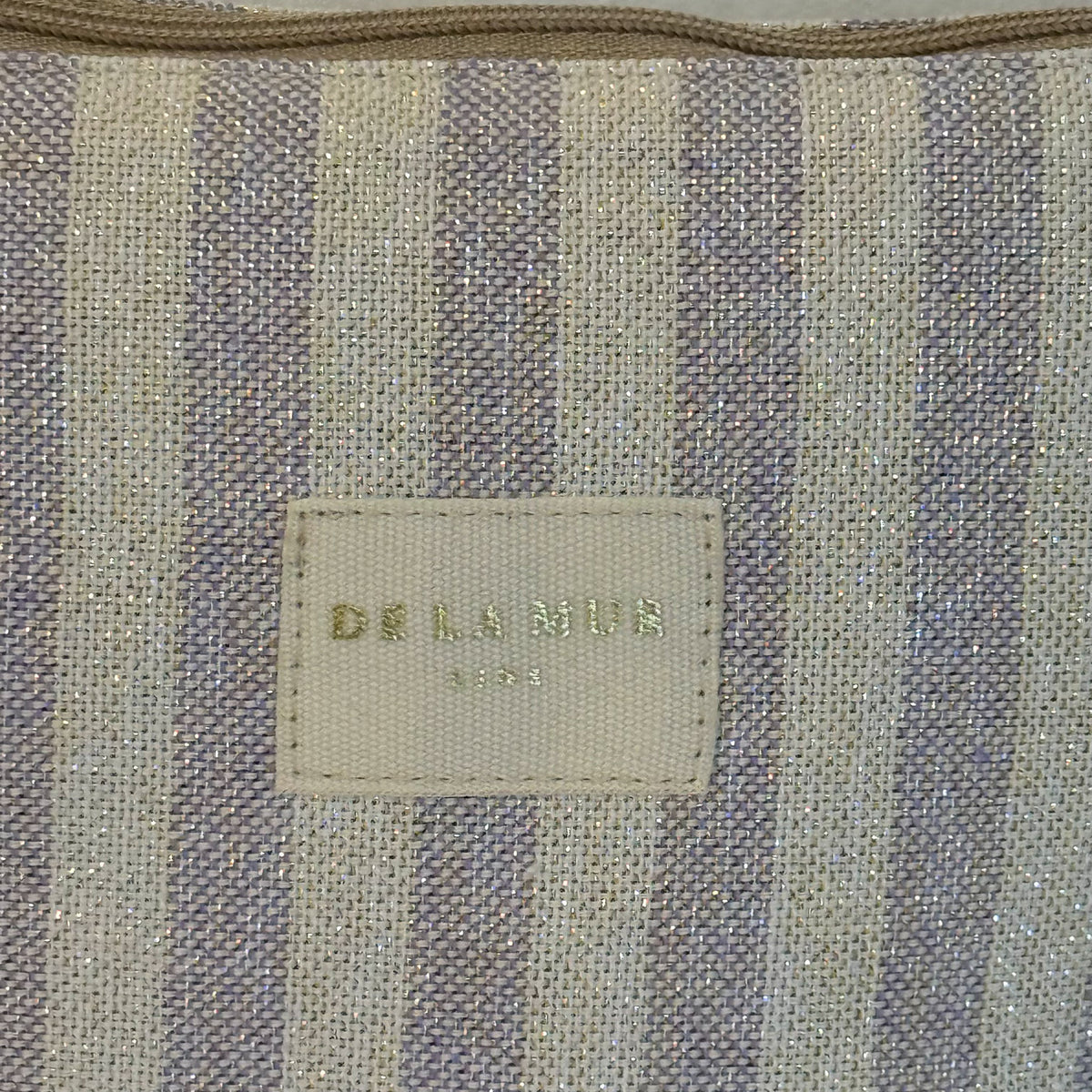 Close-up of the DE LA MUR beige and lilac striped lurex fabric and label