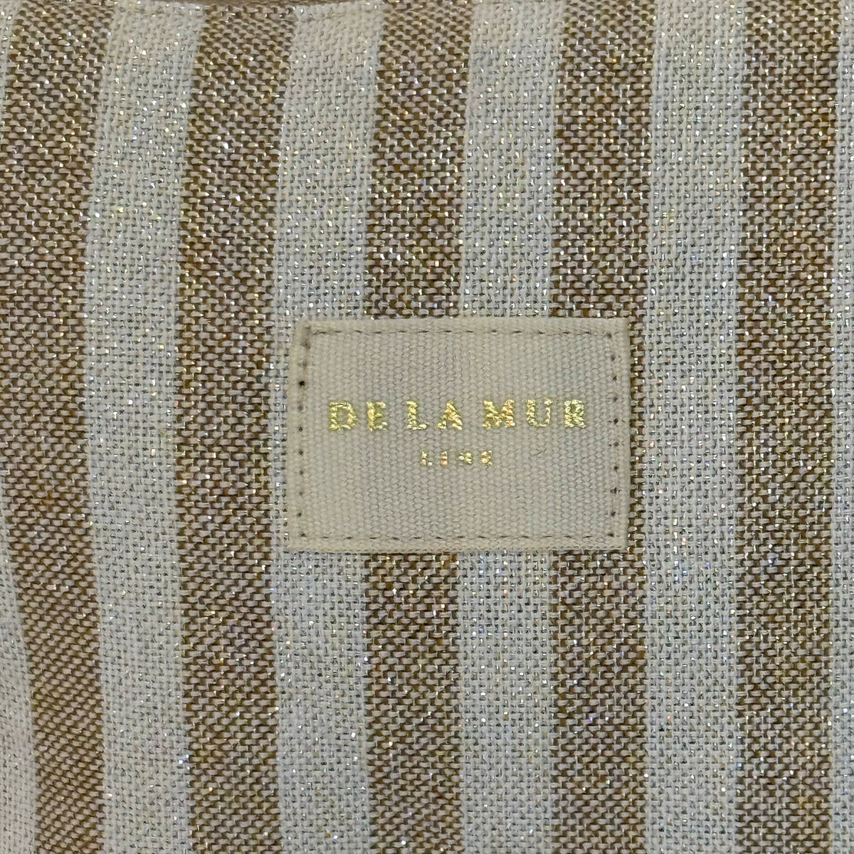 Close-up of the DE LA MUR beige and mustard striped lurex fabric and label