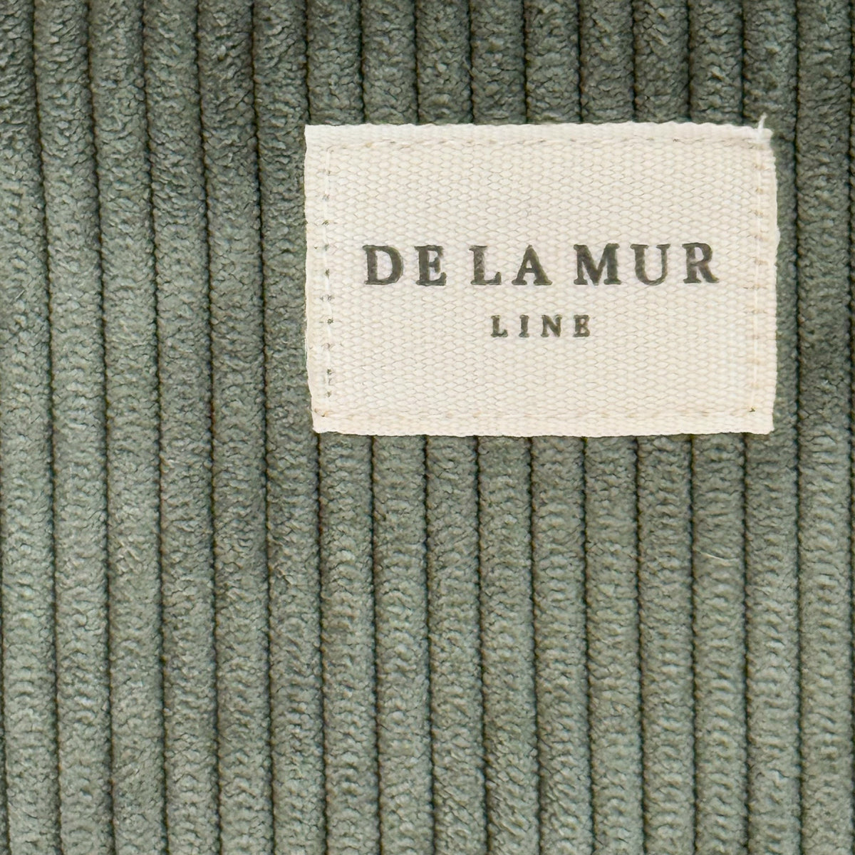 Close-up of the green corduroy ribbing and DE LA MUR Line label on the Tree phone sleeve
